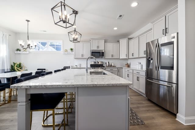 Modern kitchen with white cabinetry, gray marble island with seating, stainless steel appliances, pendant lighting, and open floor plan connecting to dining area