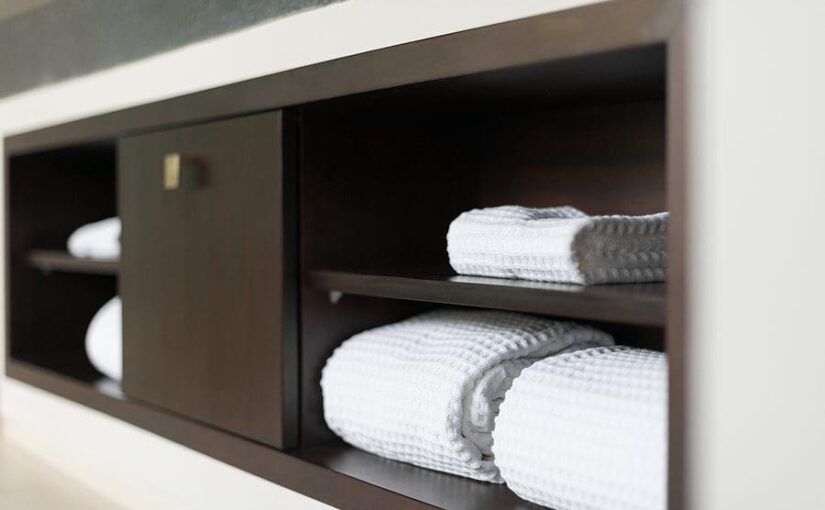 Built-in wooden bathroom shelf displaying neatly rolled white towels in a modern hotel room
