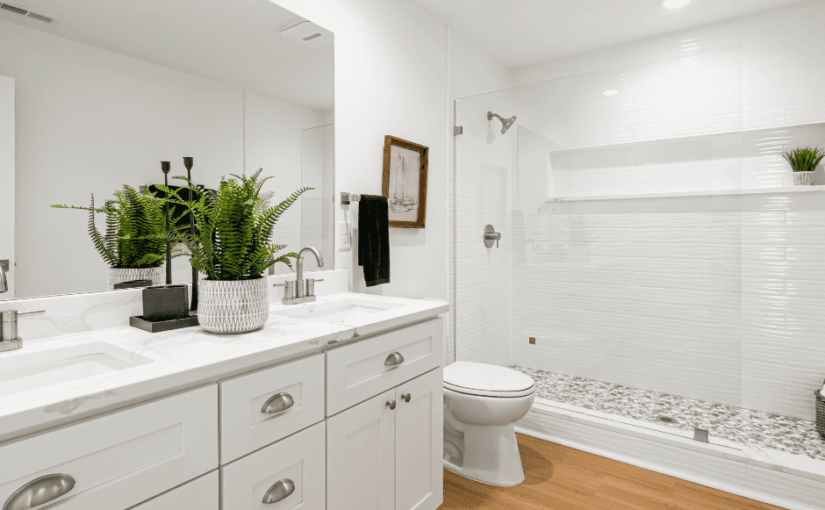 Modern white bathroom with dual vanity, marble countertop, large mirror, walk-in shower with white subway tile, wooden flooring, and potted green plants