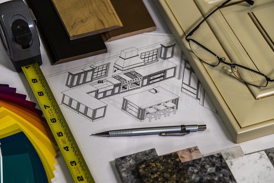 Designer's workspace with kitchen cabinet sketches, measuring tape, technical pen, material samples, and color swatches for interior remodeling project planning