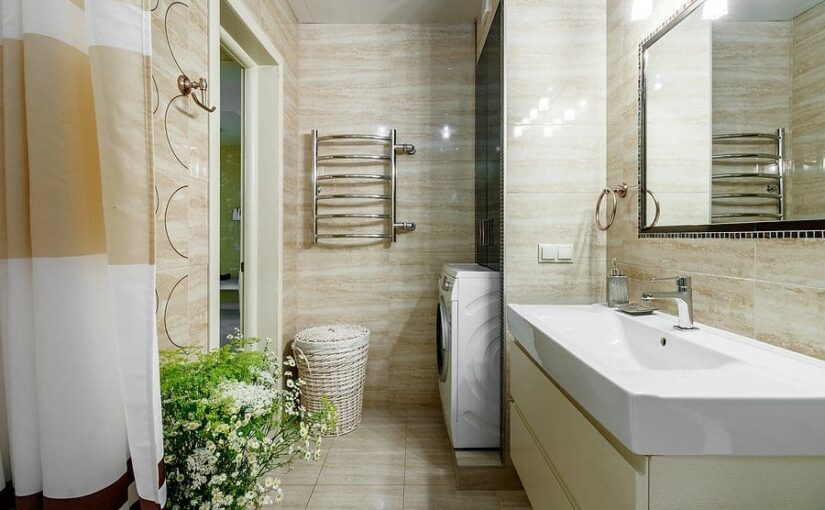 Modern bright bathroom with white vanity, large mirror, towel rack, shower with white curtain, potted plants, and beige tile flooring