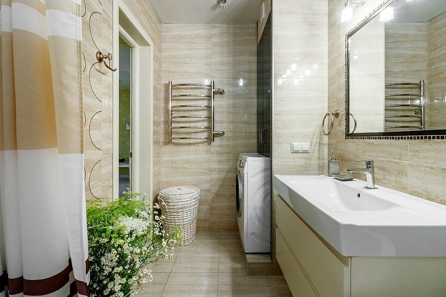 Modern bright bathroom with white vanity, large mirror, towel rack, shower with white curtain, potted plants, and beige tile flooring