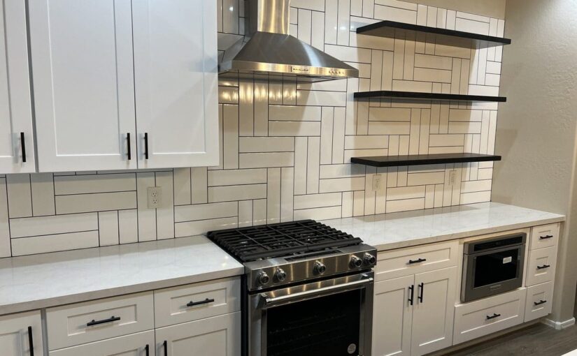 Modern kitchen with white cabinetry, stainless steel gas range, white quartz countertops, geometric subway tile backsplash, black floating shelves, and stainless steel range hood