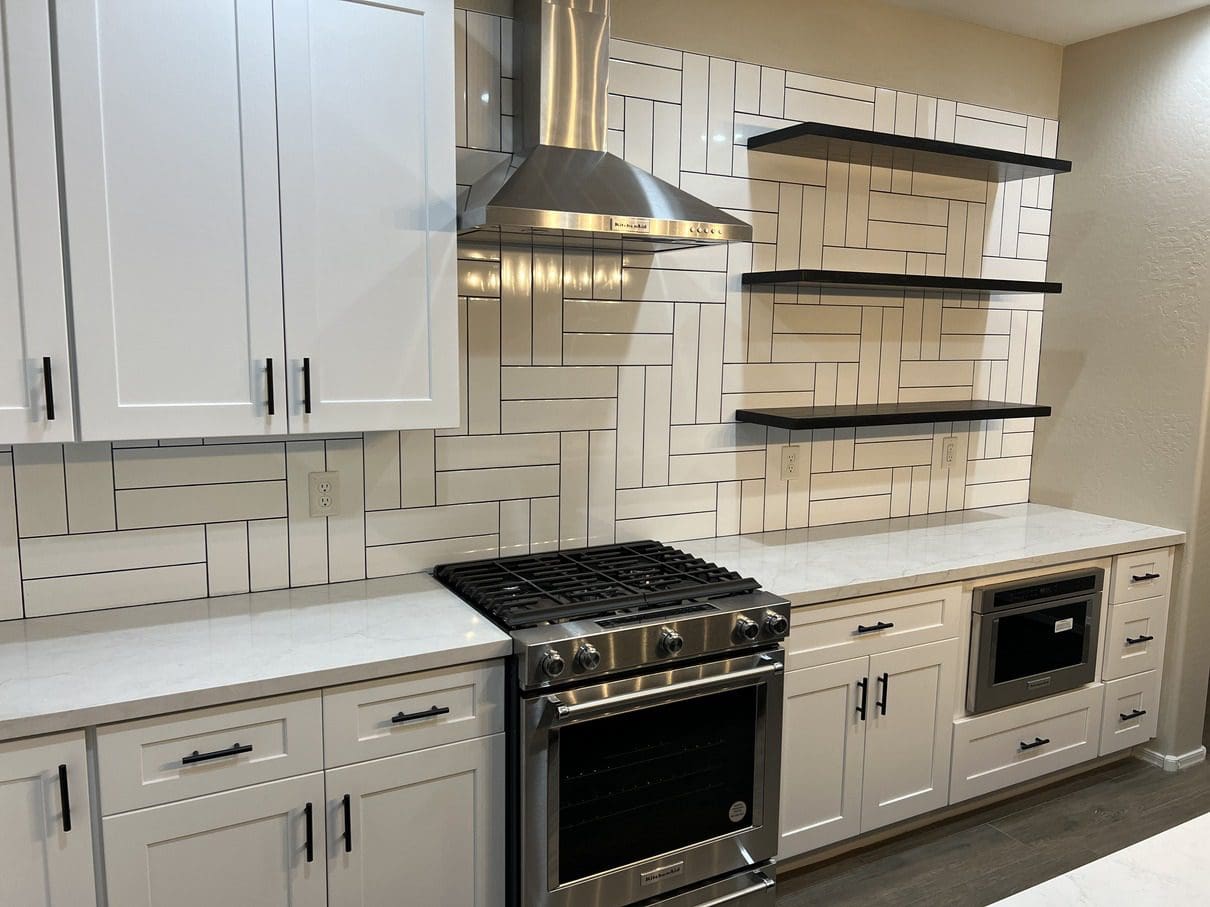 Modern kitchen with white cabinetry, stainless steel gas range, white quartz countertops, geometric subway tile backsplash, black floating shelves, and stainless steel range hood