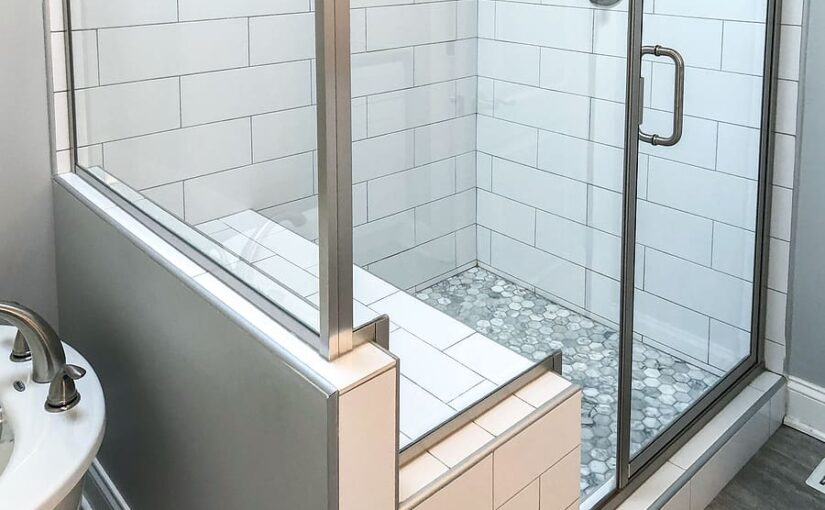 Modern bathroom shower enclosure with white subway tiles, built-in bench seat, mosaic floor tiles, and glass doors with chrome fixtures