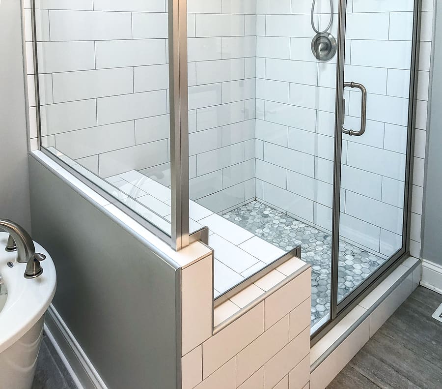 Modern bathroom shower enclosure with white subway tiles, built-in bench seat, mosaic floor tiles, and glass doors with chrome fixtures