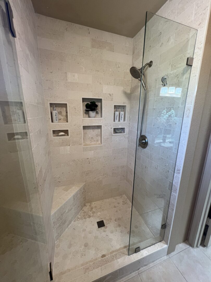 Modern luxury bathroom shower with travertine tile walls, built-in niches, rainfall showerhead, and frameless glass enclosure