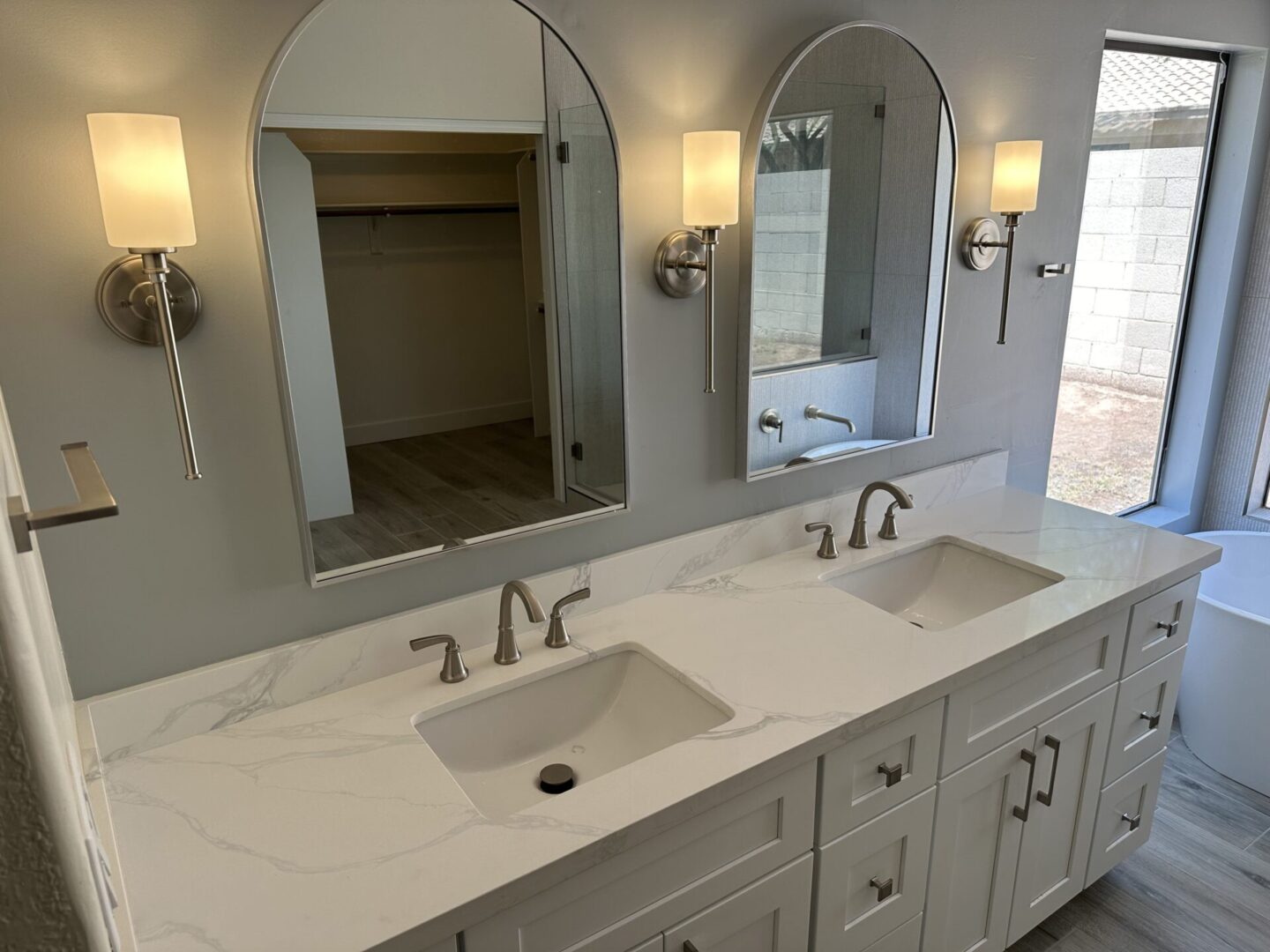 Luxurious master bathroom with double-sink vanity, white marble countertops, arched mirrors, and brushed nickel fixtures