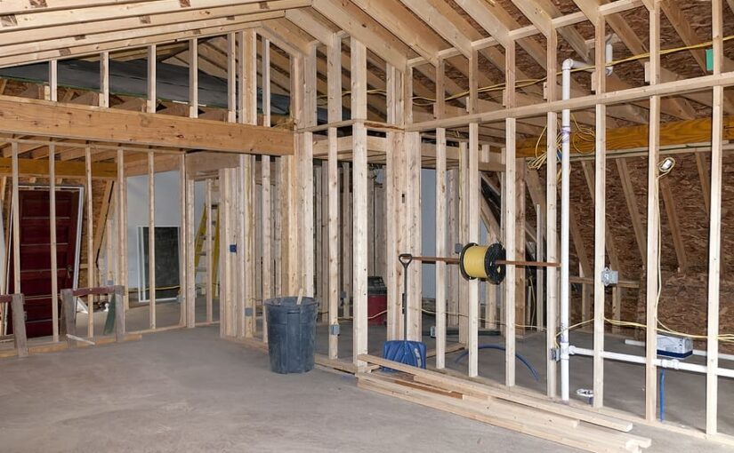 Interior framing of residential construction showing wooden studs, exposed insulation, drywall, and electrical wiring during renovation or new room addition
