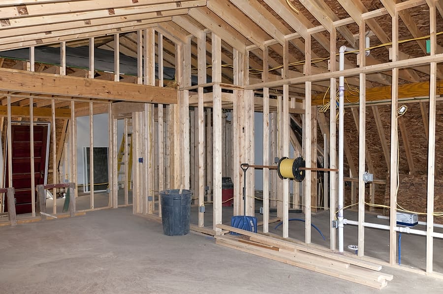 Interior framing of residential construction showing wooden studs, exposed insulation, drywall, and electrical wiring during renovation or new room addition