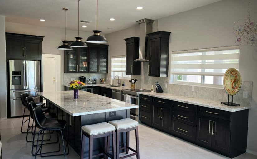 Modern kitchen with black cabinetry, marble countertops, stainless steel appliances, pendant lights over island with seating, and light gray walls