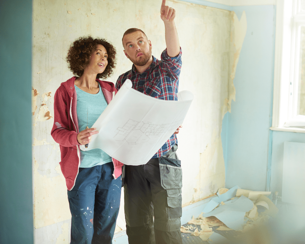 Couple reviewing blueprint in unfinished room during home renovation project