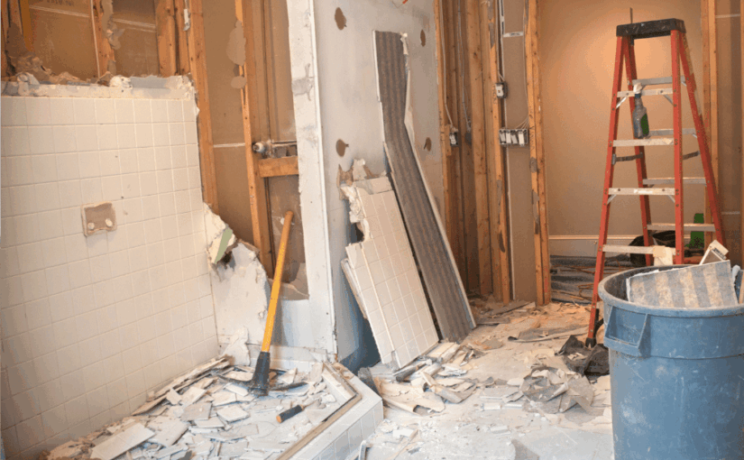 Bathroom renovation in progress with exposed framing, removed fixtures, scattered debris, a red ladder, and blue utility bucket