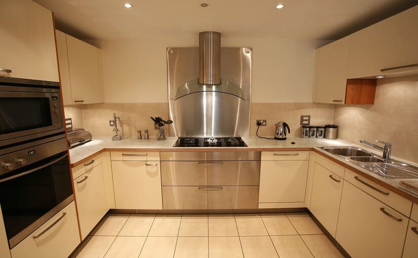 Modern kitchen with cream cabinets, stainless steel appliances, gas cooktop with range hood, built-in microwave, and tile flooring in U-shaped layout