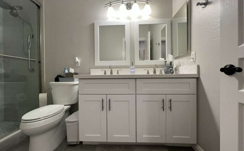Modern bathroom with white vanity cabinets, dual sinks, framed mirrors, chrome fixtures, and glass shower enclosure