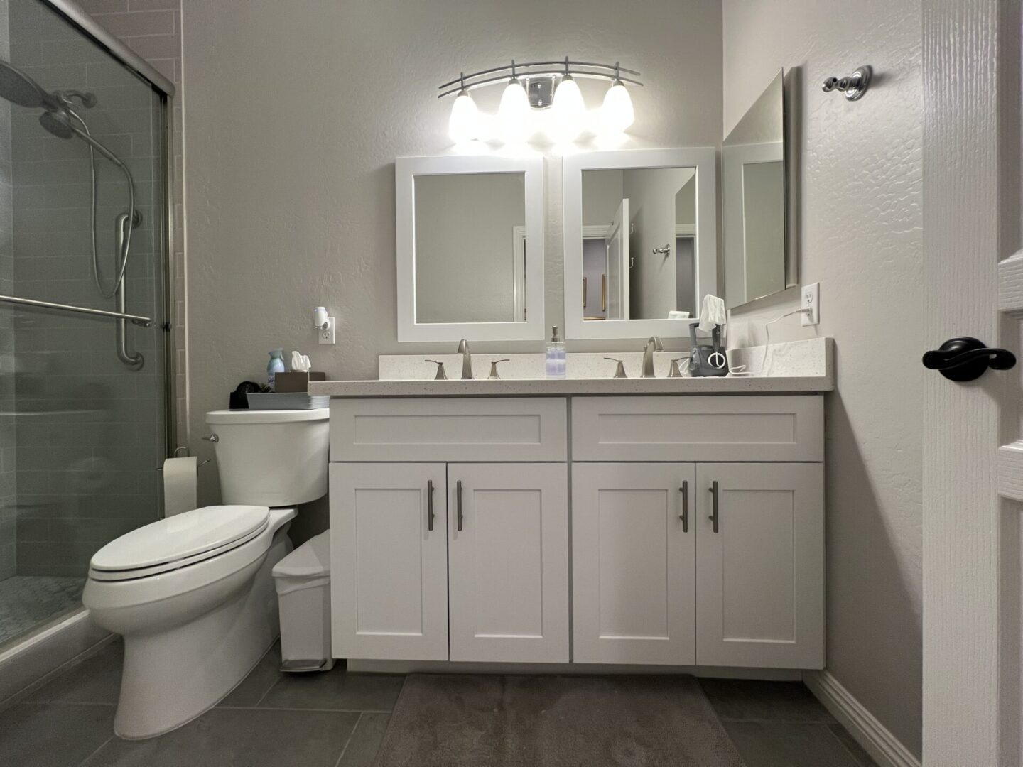 Modern bathroom with white vanity cabinets, dual sinks, framed mirrors, chrome fixtures, and glass shower enclosure