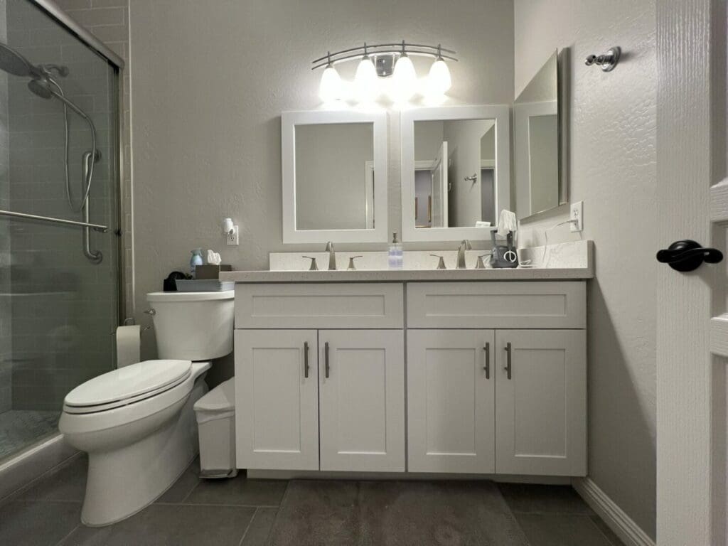 Modern bathroom with dual white vanity, two framed mirrors, chrome fixtures, and a walk-in shower with glass enclosure