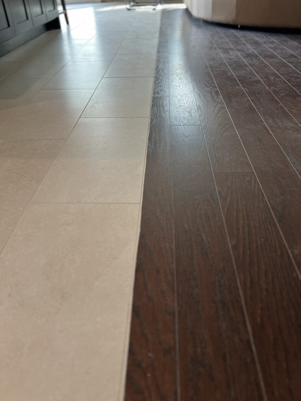 Interior floor showing transition between light beige tile and dark wood-grain laminate flooring in a modern space