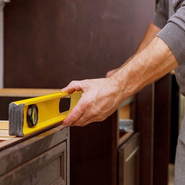 Carpenter's hand holding yellow level against wooden cabinet during kitchen installation or renovation