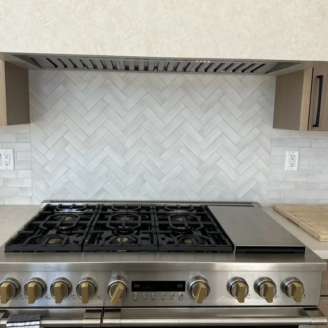 Professional kitchen with stainless steel gas range and white herringbone tile backsplash